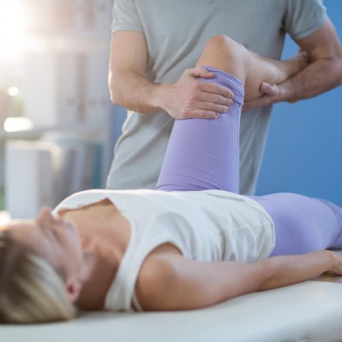 Male physiotherapist giving knee massage to female patient in clinic